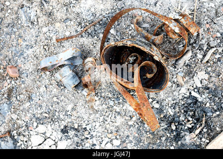 Burnt food can aged with rust sits in the ash remains of a fire Stock Photo