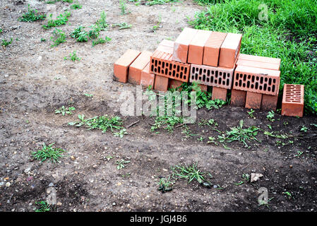 Pile of red construction bricks forgotten and left abandoned on a wasteland background with grass and dry mud Stock Photo