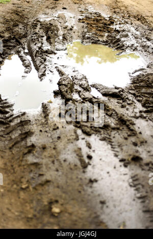 Rain filled muddy puddle with vehicle tracks on a dirt track road Stock Photo