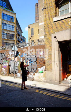 Person taking photographs of the graffiti in Corbet Place near Brick Lane, Shoreditch, London E1 using her smartphone Stock Photo