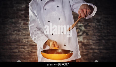 Closeup of chef cooker ready to cook, holding empty grill pan, flying motion effect. Ready for product placement. Old brick wall on background Stock Photo