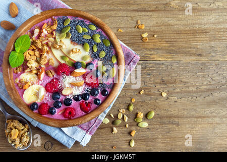 Healthy breakfast smoothie bowl topped with fruits, nuts, berries and seeds over rustic wooden background with copy space Stock Photo