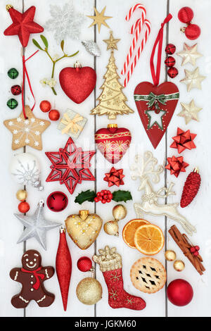 Christmas symbols with bauble decorations, holly, mistletoe, mince pie, gingerbread biscuit  and chocolate candy on distressed white wood background. Stock Photo