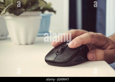 Black computer mouse in the hand of man on the white Desk. Working in the office on laptop business concept. close-up Stock Photo