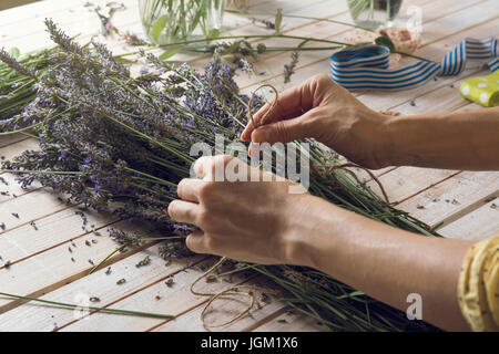 Florist at work: woman creating bouquet of natural lavender flowers, tying the flowers with a rope in te wooden table, small business concept. Close-u Stock Photo