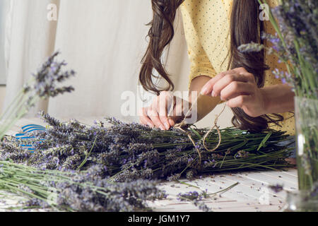 Florist at work: woman creating bouquet of natural lavender flowers, tying the flowers with a rope in te wooden table, small business concept. Close-u Stock Photo