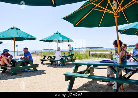 Wellfleet, USA - July 30, 2014: People sitting on tables eating lunch by beach shore in village in Cape Cod Stock Photo