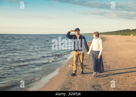 elderly couple having romantic walk on the beach at sunset