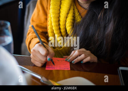 Girl with painted nails writing on a post-it note Stock Photo