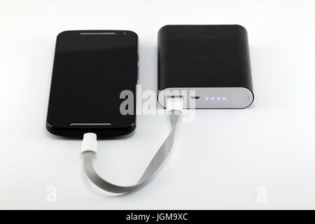Smartphone charging from black power bank isolated on white background. Smartphone and power bank concept. Stock Photo