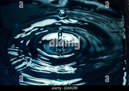 Water drop splashing into smooth water causing ripples in a calm surface Stock Photo