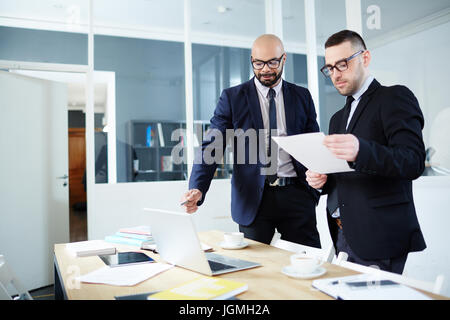 Traders analyzing online data and papers in office Stock Photo