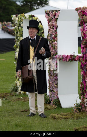 Man talking, is dressed in Victorian outfit & standing by giant floral RHS letters - RHS Chatsworth Flower Show showground, Derbyshire, England, UK. Stock Photo