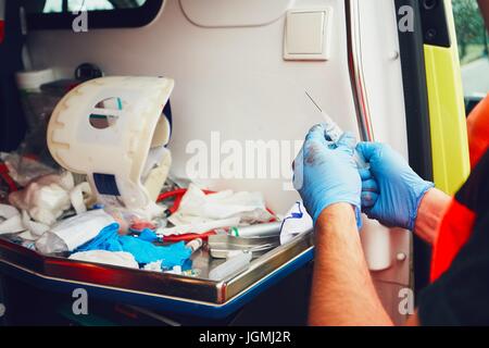 Paramedic in door of the ambulance car prepares medicines for an injured patient (detail of the hands). Theme of the rescue, help and hope. Stock Photo