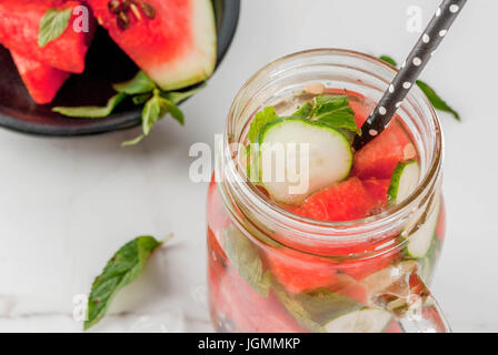 Summer drinks and cocktails. Lemonade, infused detox water with mints, fresh watermelon and cucumber. In mason jar, on a white marble table. Copy spac Stock Photo