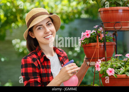 portrait of happy young woman gardener spraying water on plants. Girl with sprayer bottle spraying pesticide on her flowers. People, gardening, care o Stock Photo