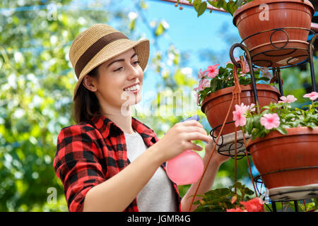 portrait of happy young woman gardener spraying water on plants. Girl with sprayer bottle spraying pesticide on her flowers. People, gardening, care o Stock Photo