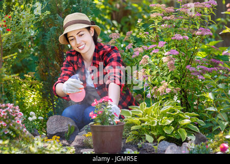 portrait of happy young woman gardener spraying water on plants. Girl with sprayer bottle spraying pesticide on her flowers. People, gardening, care o Stock Photo