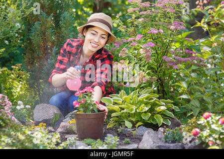 portrait of happy young woman gardener spraying water on plants. Girl with sprayer bottle spraying pesticide on her flowers. People, gardening, care o Stock Photo