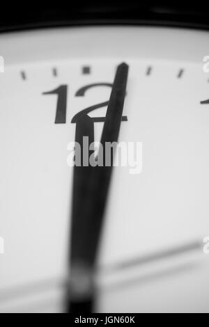 Closeup and selective on the pointers of a clock marking a minute after midnight - black and white rendering. The main focus is on the number twelve a Stock Photo