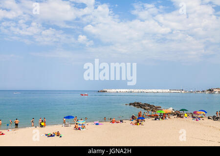 GIARDINI NAXOS, ITALY - JUNE 27, 2017: tourists on urban beach in Giardini-Naxos town and view of city port. Giardini Naxos is seaside resort on Ionia Stock Photo