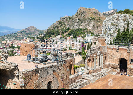 TAORMINA, ITALY - JUNE 29, 2017: tourists in Teatro antico, ancient Greek Theater (Teatro Greco) and view of Taormina city on mountain slope. The amph Stock Photo