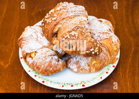 three fresh italian croissants filled by vanilla and chocolate creams on wooden table Stock Photo