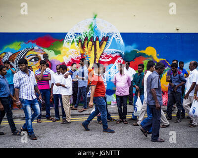 July 9, 2017 - Singapore, Singapore - Guest worker from the Indian sub-continent in front of a mural in Singapore. There are hundreds of thousands of guest workers from the Indian sub-continent in Singapore. Most work 5 Â½ to six days per week. On Sundays, the normal day off, they come into Singapore's ''Little India'' neighborhood to eat, drink, send money home, go to doctors and dentists and socialize. Most of the workers live in dormitory style housing far from central Singapore and Sunday is the only day they have away from their job sites. Most work in blue collar fields, like constructio Stock Photo