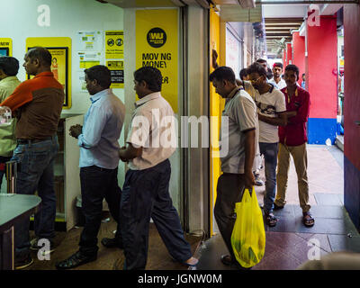 July 9, 2017 - Singapore, Singapore - Guest workers from the Indian sub-continent line up to get into a Western Union to send money back to their families. There are hundreds of thousands of guest workers from the Indian sub-continent in Singapore. Most work 5 Â½ to six days per week. On Sundays, the normal day off, they come into Singapore's ''Little India'' neighborhood to eat, drink, send money home, go to doctors and dentists and socialize. Most of the workers live in dormitory style housing far from central Singapore and Sunday is the only day they have away from their job sites. Most wor Stock Photo