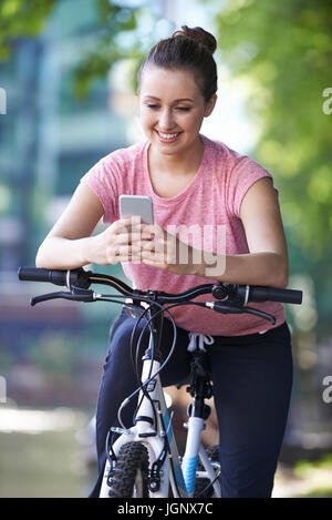 Young Woman Using Mobile Phone Whilst Out On Cycle Ride Stock Photo