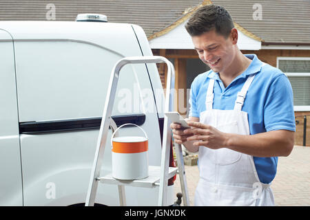 Decorator Using Mobile Phone Standing Outside Domestic Home Stock Photo
