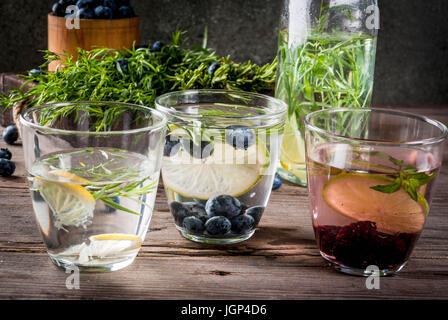 Summer refreshment diet drinks. Infused detox waters in different glasses nd bottles with rosemary, lime and blueberries, lemon and tarragon, blackber Stock Photo