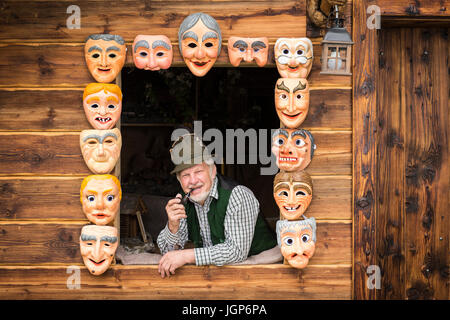 Wooden mask carver in a window, framed by painted wooden masks, wooden mask carving workshop, Bad Aussee, Styria, Austria Stock Photo