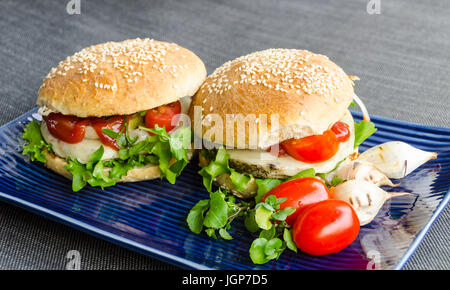 Two beluga lentils and hemp seed burgers, stacked with homegrown salad, onion rings, tomatoes, in homemade rye buns with sesame seeds. Stock Photo