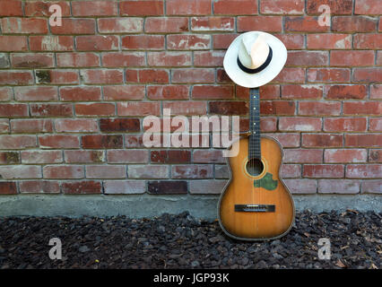 Guitar player takes a break leaving old acoustic guitar, Blues Harp and Panama Hat leaning against a brick wall. Stock Photo
