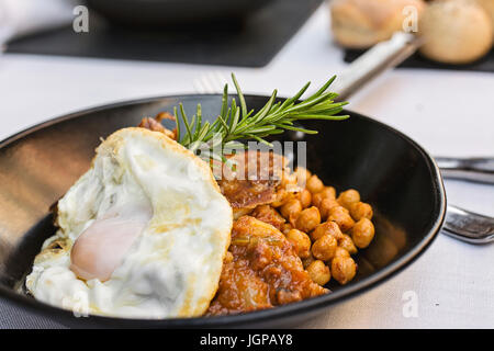 Meat with fried egg and chickpeas, in individual pan, on set table Stock Photo