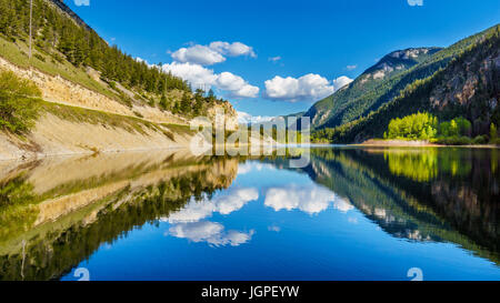 Blue sky, trees and mountains reflecting in the smooth surface on the crystal clear water of Crown Lake, along Highway 99 in Marble Canyon, BC, Canada Stock Photo