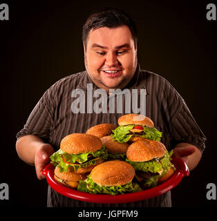 Fat man eating fast food hamberger and carries treat for friends on tray. Breakfast for overweight person. Junk meal leads to obesity. Stock Photo