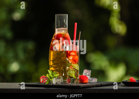Homemade strawberry ice tea in the garden. Strawberries, mint and lemon balm leaves, ice and green tea. Stock Photo