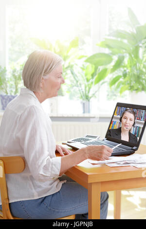 Senior woman at home with her laptop and lots of receipts, listening to an accountant before making her annual tax declaration, online tax advice conc Stock Photo