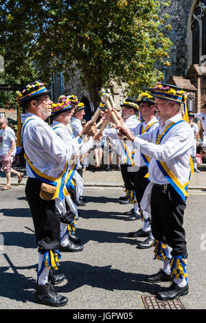 Traditional English folk dancers, Yateley Morris side dancing in the street in the medieval town, Sandwich during folk and ale festival. Standing in two rows, crossing wooden poles. Stock Photo