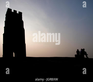 Three young people sat on Glastonbury Tor in the early evening, Glastonbury, Somerset, UK Stock Photo