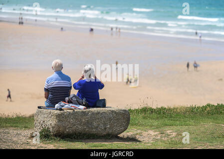 Two elderly holidaymakers sitting on a rock on the Headland overlooking Fistral Beach in Newquay, Cornwall. Stock Photo