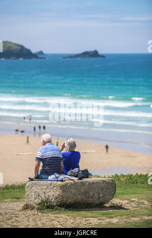 Two elderly holidaymakers sitting on a rock on the Headland overlooking Fistral Beach in Newquay, Cornwall. Stock Photo