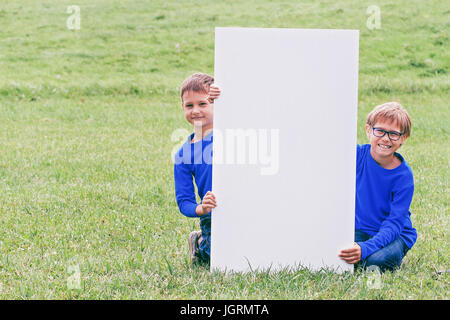 Boy sitting on the grass with vertical blank white placard board outdoors Stock Photo