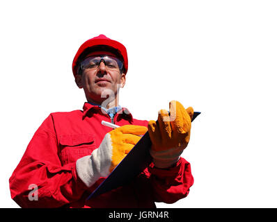 Worker wearing red overalls and hardhat , writing on clipboard next to pipelines, isolated on white. Stock Photo