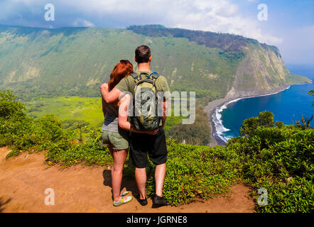 Hikers by road into Waipio Valley on the Big Island of Hawaii see black sand beach and beyond Stock Photo