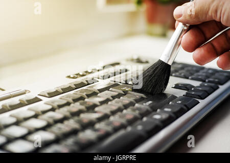 Cleaning keyboard from dust by black brush. Cleaning concept. Office cleaning. Stock Photo