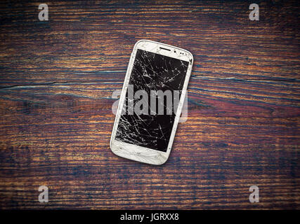 Phone with a broken display on a wooden table. Broken smartphone. Stock Photo