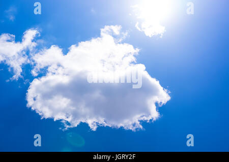 The sun is bright shining blue through a small cloud. Cumulus clouds in the blue sky. The sun shines through white cloud. Stock Photo